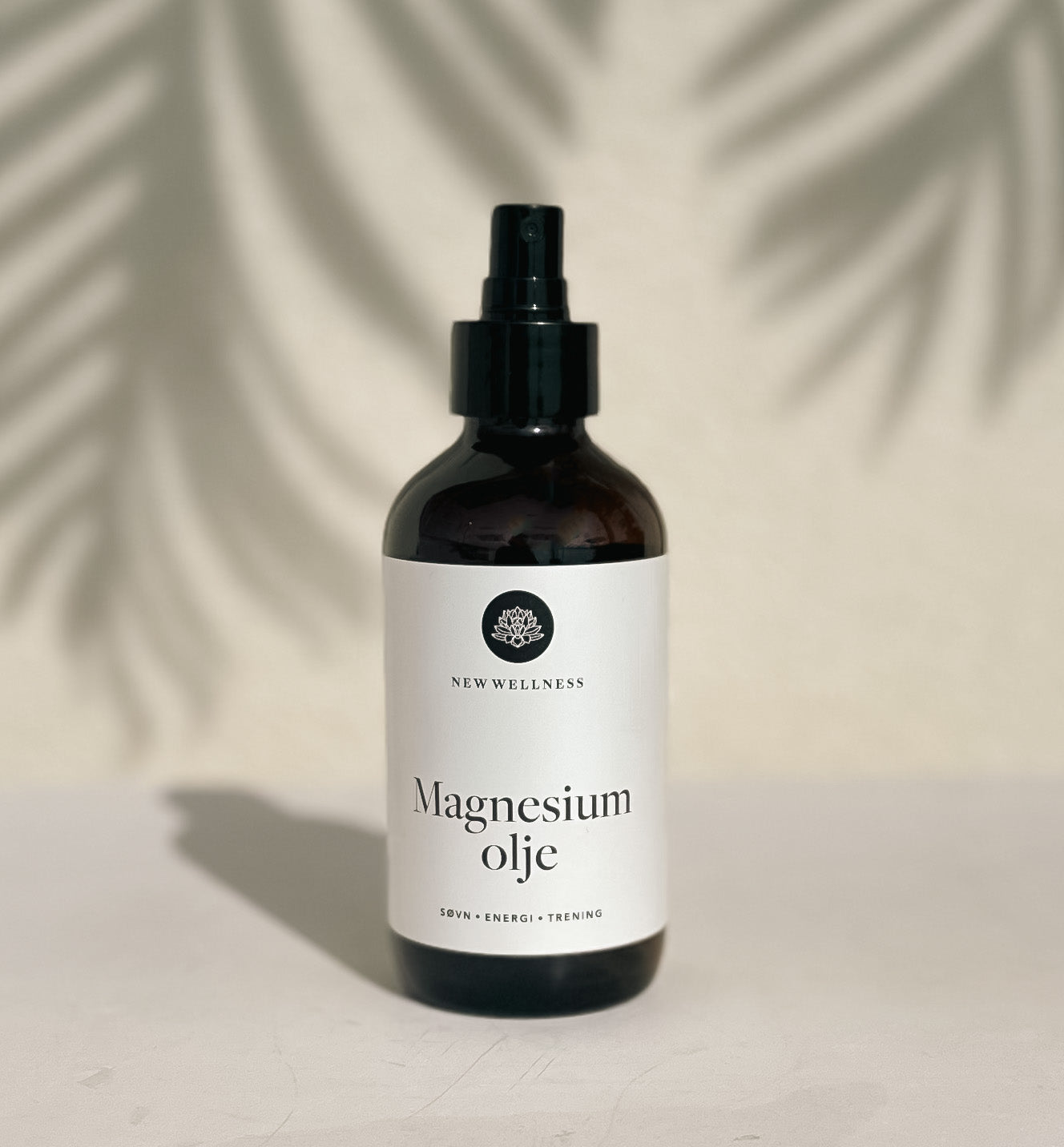 New Wellness magnesiumolje mørkebrun glassflaske med sort spraypumpe. Etiketten er hvit, og designet er elegant.